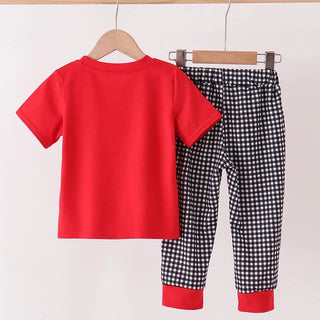 A two-piece children's outfit set hanging on wooden hangers from a light wood rod. The set includes a solid bright red short-sleeve t-shirt and black-and-white gingham checkered pants with solid red cuffs.