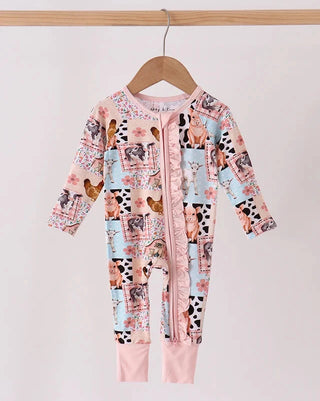 A baby long-sleeve footless sleeper jumpsuit hanging on a wooden hanger against a light pink background. The garment features a colorful collage print of farm animals (chickens, cows, pigs, sheep) on a light blue and pink base, with solid light pink cuffs and a matching pink ruffle trim along the front zipper.