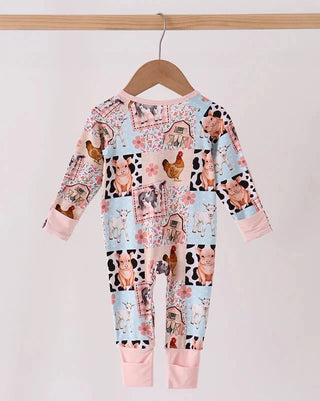 A baby long-sleeve footless one-piece jumpsuit with a colorful farm animal patchwork print, hanging on a wooden hanger against a plain white wall.