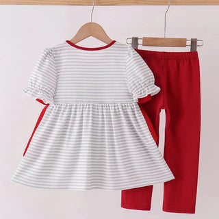 A toddler girl's two-piece clothing set hanging on wooden hangers from a wooden rod. The set includes a white short-sleeve dress with thin gray horizontal stripes, red trim at the collar and side details, and solid red leggings.