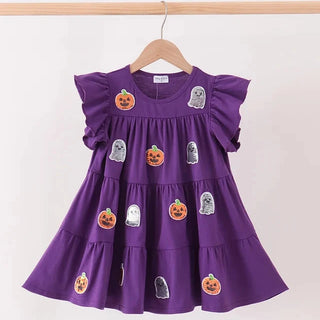 A purple tiered baby dress with ruffled sleeves, decorated with Halloween-themed embroidered patches of pumpkins and ghosts, hanging on a wooden hanger against a plain white wall.