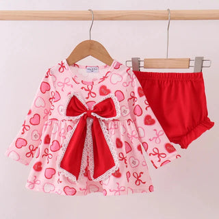 Baby outfit with pink dress and red bloomers on a hanger against a white background