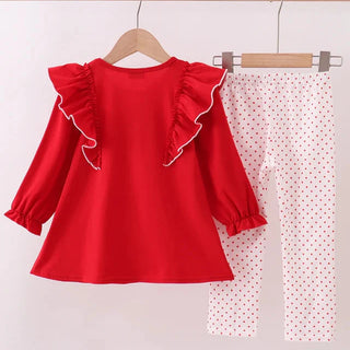Red blouse with ruffled sleeves and white pants with red polka dots on a wooden rack.