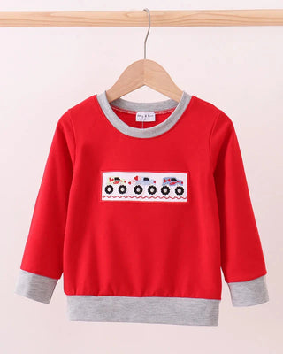 Red children's sweatshirt with a graphic on a wooden hanger against a light pink background