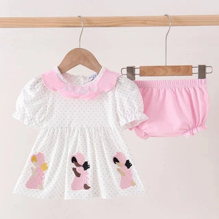 A baby girl's two-piece outfit set hanging on wooden hangers against a light pink wall. The set includes a white short-sleeve dress with a pink collar and pink embroidered characters on the skirt, paired with matching pink bloomers.