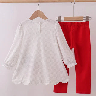 White blouse and red pants hanging on a rack against a white background