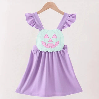 A toddler girl's lavender dress with ruffled shoulder straps and a light green pumpkin applique on the chest featuring pink facial details, hanging on a wooden hanger.