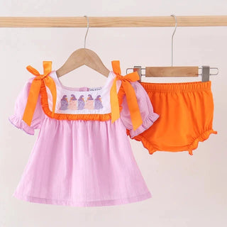 A baby girl's two-piece outfit set consisting of a light pink dress with orange trim and bows, and matching orange bloomers, hanging on wooden hangers against a plain light background.