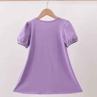 A lavender purple short-sleeve tunic top with puffed sleeves and green trim, hanging on a wooden hanger against a plain light background.