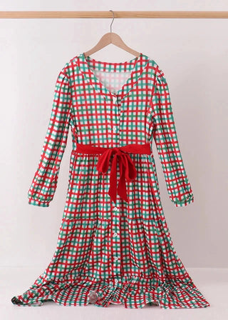 A long-sleeve tiered dress with a red and green gingham plaid pattern, featuring a red tie belt at the waist, hanging on a wooden hanger against a light gray background.