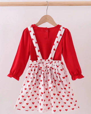 Red long-sleeve top with white apron dress featuring red heart patterns on a beige background.