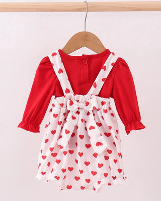 Red long-sleeve top with white baby bubble featuring red heart patterns on a wooden hanger against a light pink background.