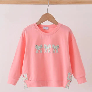 A pink long-sleeve sweatshirt with embroidered bow and floral details, hanging on a wooden hanger against a light pink background.