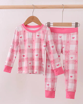 Pink children's pajama set with hearts and bows on a hanger against a white background