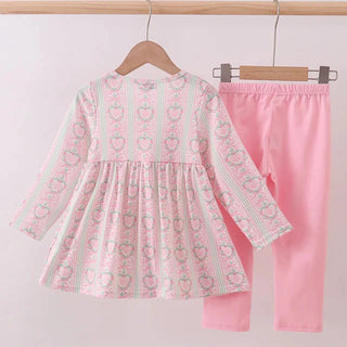 Pink shirt with heart patterns and pink pants on a wooden hanger against a white background