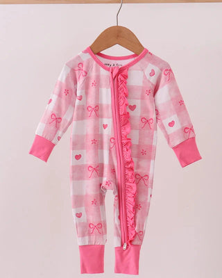 Pink baby onesie with bow and heart patterns on a hanger against a light pink background