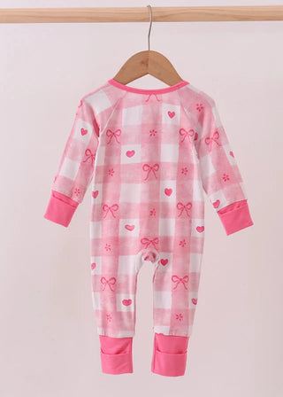 Pink and white baby onesie with heart and bow patterns on a hanger against a light pink background.