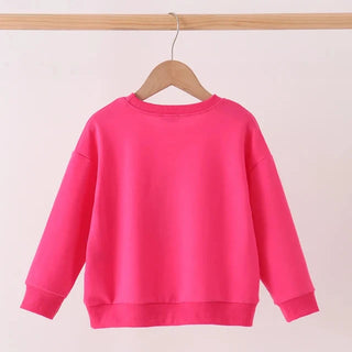 A bright pink long-sleeve crewneck sweatshirt hanging on a wooden hanger from a light wood rod, set against a plain off-white background.