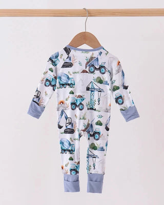 A baby long-sleeve footless jumpsuit with an all-over construction vehicle print, hanging on a wooden hanger from a light wood rod against a plain off-white background.