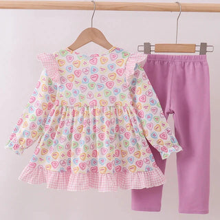 Children's shirt with heart pattern and purple pants on hangers against a light background