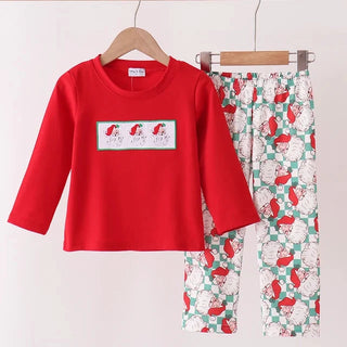 A children's two-piece pants set hanging on wooden hangers against a plain light background. The set includes a bright red long-sleeve top with a rectangular Santa graphic on the chest, and matching green patterned pants with white snowflakes and red Santa hats.