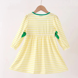 A yellow and white striped long-sleeve dress with green trim and green ribbon bows on the sleeves, hanging on a wooden hanger against a plain light background.