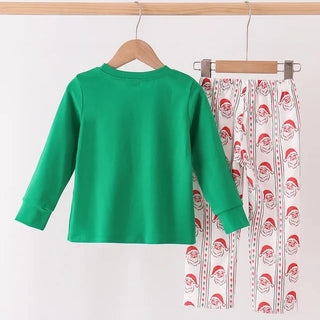 A children's two-piece pants set hanging on wooden hangers against a plain white wall. The set includes a bright green long-sleeve top and white pants with a red and green Santa Claus pattern.