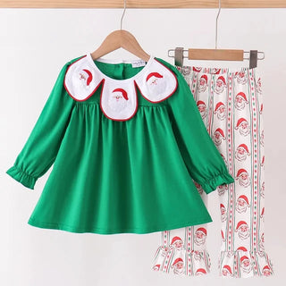 A children's two-piece outfit hanging on wooden hangers against a plain light background. The set includes a bright green long-sleeve top with three white Peter Pan-style collar patches featuring Santa faces, and matching white pants printed with Santa faces and red stripes.