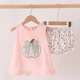 A light pink sleeveless baby top with a pumpkin applique on the front, shown hanging on a wooden hanger next to  matching patterned bloomers  on a white background.