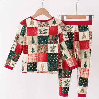 A two-piece children's pajama set featuring a long-sleeve top and matching pants in a festive Christmas patchwork print, hanging on wooden hangers against a plain white background.
