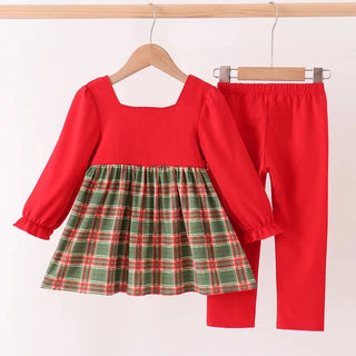 A toddler girl's two-piece outfit set consisting of a red long-sleeve dress with a green and red plaid skirt and matching red leggings, hanging on wooden hangers against a plain white wall.