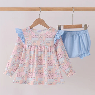 A toddler girl's two-piece outfit hanging on wooden hangers against a plain light background. The set includes a long-sleeve smocked dress in a pink and light blue patchwork floral print with light blue ruffle shoulder straps, and a pair of light blue bloomers.