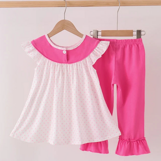 A toddler girl's two-piece outfit hanging on wooden hangers from a wooden rod. The set includes a white short-sleeve top with a bright pink ruffled collar and a tiny polka dot pattern, paired with bright pink leggings featuring ruffled cuffs.