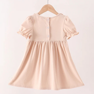 A light beige short-sleeve dress with puff sleeves and a buttoned neckline, hanging on a wooden hanger against a plain light background.