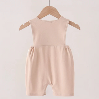 A sleeveless baby romper in a soft khaki color, hanging on a wooden hanger from a wooden clothes rack against a plain off-white background.