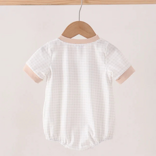A short-sleeve baby romper hanging on a wooden hanger from a light wood rod, featuring a white and beige gingham pattern with solid beige trim on the collar and sleeve cuffs.