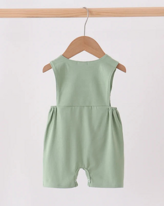 A sage green sleeveless baby romper hanging on a wooden hanger from a light wood rod against a plain white background.
