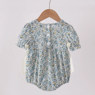 A baby girl's short-sleeve romper with a blue and yellow floral print, hanging on a wooden hanger from a light wood rod against a plain off-white background.