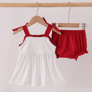 A two-piece toddler girl's summer outfit set hanging on wooden hangers from a wooden rod. The set includes a white sleeveless top with red ruffled straps and a white micro-dot pattern, paired with bright red ruffled-border bloomers.