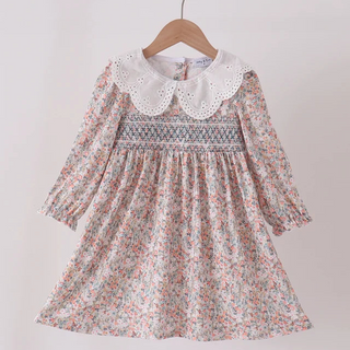 A young girl's long-sleeve dress with a delicate pink, green, and blue floral print, featuring a white lace Peter Pan collar and a smocked bodice, hanging on a wooden hanger against a plain light background.