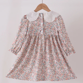 A young girl's long-sleeve dress with a dense small floral print in pink, blue, and green on a light background, featuring a contrasting white eyelet Peter Pan collar and buttoned neckline, hanging on a wooden hanger.