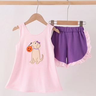 A children's two-piece shorts set hanging on wooden hangers against a plain light background. The set includes a light pink gingham sleeveless top with an embroidered puppy holding an orange pumpkin, and matching purple shorts with white ruffle trim.