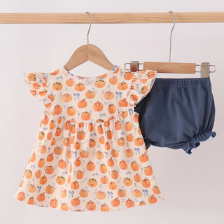 A baby girl's two-piece outfit hanging on wooden hangers from a wooden clothes rack. The set includes a short-sleeve cream dress with an orange pumpkin print and navy blue bloomers.