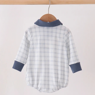 A baby long-sleeve romper hanging on a wooden hanger from a wooden clothes rack. The romper features a white and light blue plaid pattern with solid navy blue collar and cuff accents.