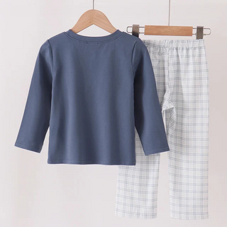 A two-piece children's pants set hanging on wooden hangers from a wooden rod. The set includes a slate blue long-sleeve top and light blue and white plaid pajama pants.