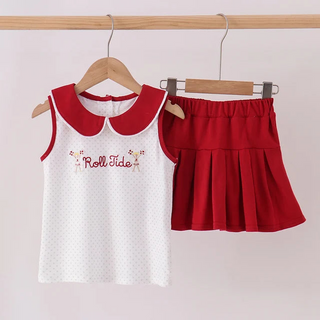 A two-piece children's outfit hanging on wooden hangers against a light pink wall. The set includes a white sleeveless top with a red Peter Pan collar and 'Roll Tide' text, paired with a red pleated mini skirt.