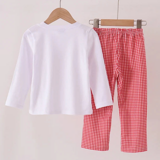A children's two-piece clothing set hanging on a wooden hanger bar. The set includes a plain white long-sleeve top on a wooden hanger and red-and-white gingham checkered pants on metal clips.