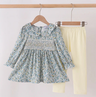A toddler girl's two-piece outfit hanging on wooden hangers against a plain light background. The set includes a long-sleeve smocked blouse in a blue and yellow floral print with a Peter Pan collar, and solid pale yellow leggings.
