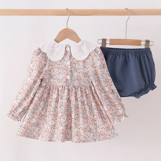A toddler girl's two-piece outfit hanging on wooden hangers from a light wood rack. The set includes a long-sleeve floral print dress with a white lace Peter Pan collar, and a pair of navy blue ruffled bloomers.