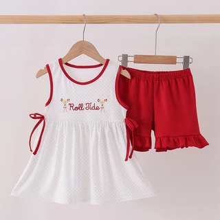 A toddler girl's two-piece summer outfit hanging on wooden hangers from a wooden rod. The set includes a white sleeveless dress with red trim and 'Roll Skates' embroidered on the chest, and matching red ruffle-hem shorts.